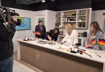 Will Aiello, Chef Trisha Donaldson, Melissa Lamb, and Marianne Long standing behind a counter on the set of CTV News Your Morning Kitchen. A camera operator is filming them.
