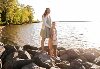 Lindsey standing with her two sons on rocks by a lake