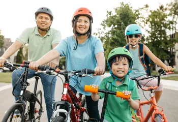 A happy family of four wearing helmets are biking outdoors.