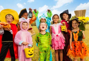 Eight children in various Halloween costumes posing in a field