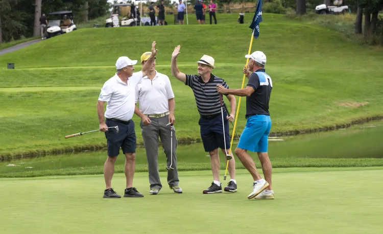 Four golfers on a golf course, two of them are high fiving