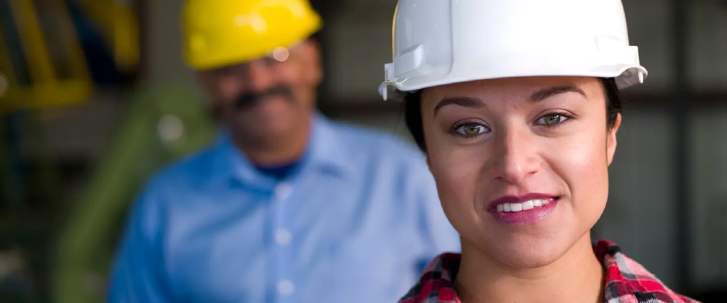 A woman wearing a white hard hat looks into the camera.