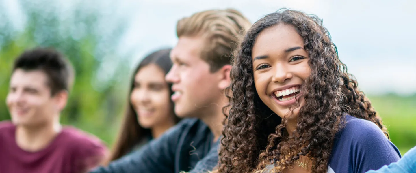 A diverse group of smiling young people sitting together outside.