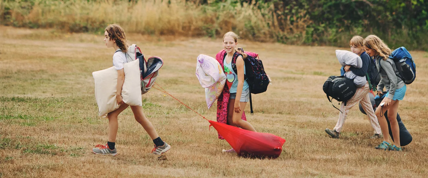 A group of campers carry pillows and sleeping bags.