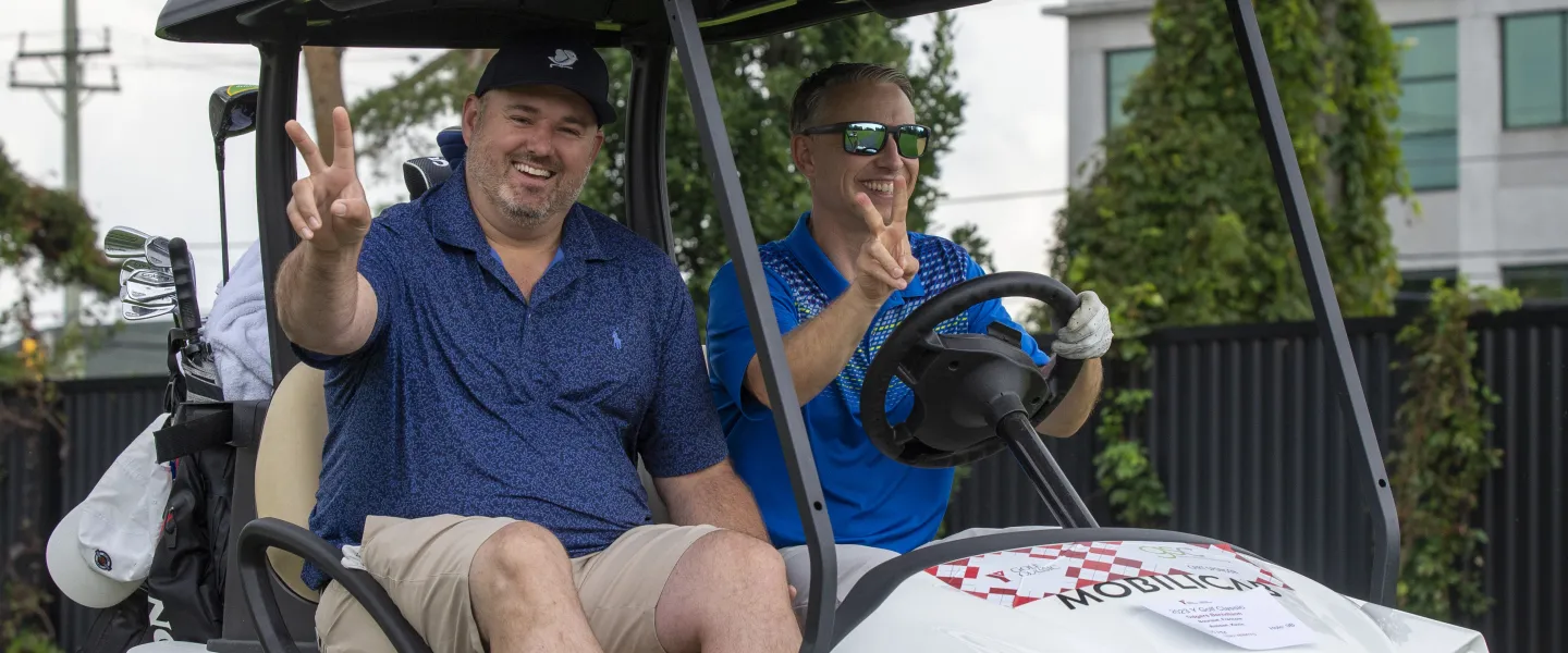 Two men holding on peace signs on a golf cart