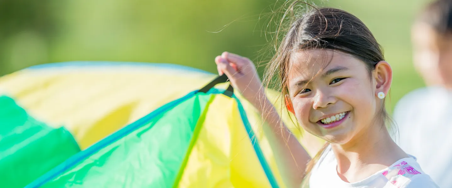 A girl holding up a section of a parachute participates in outdoor camp activities.