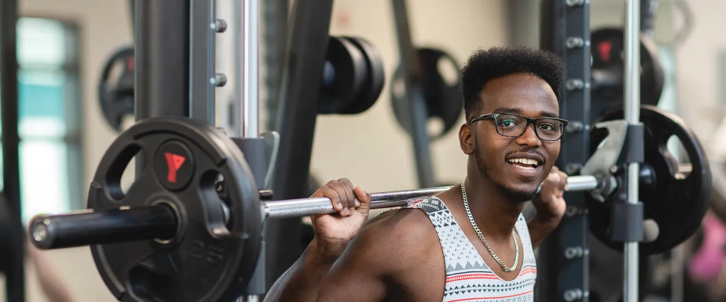 A young man holding up a barbell over his shoulder