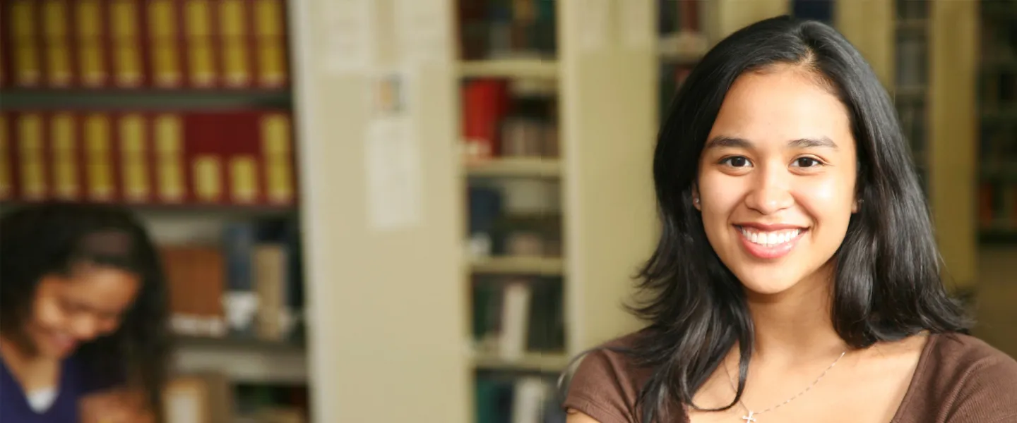 A young woman holding books in a library setting.