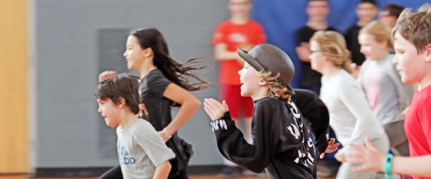 A group of children run in a gymnasium.