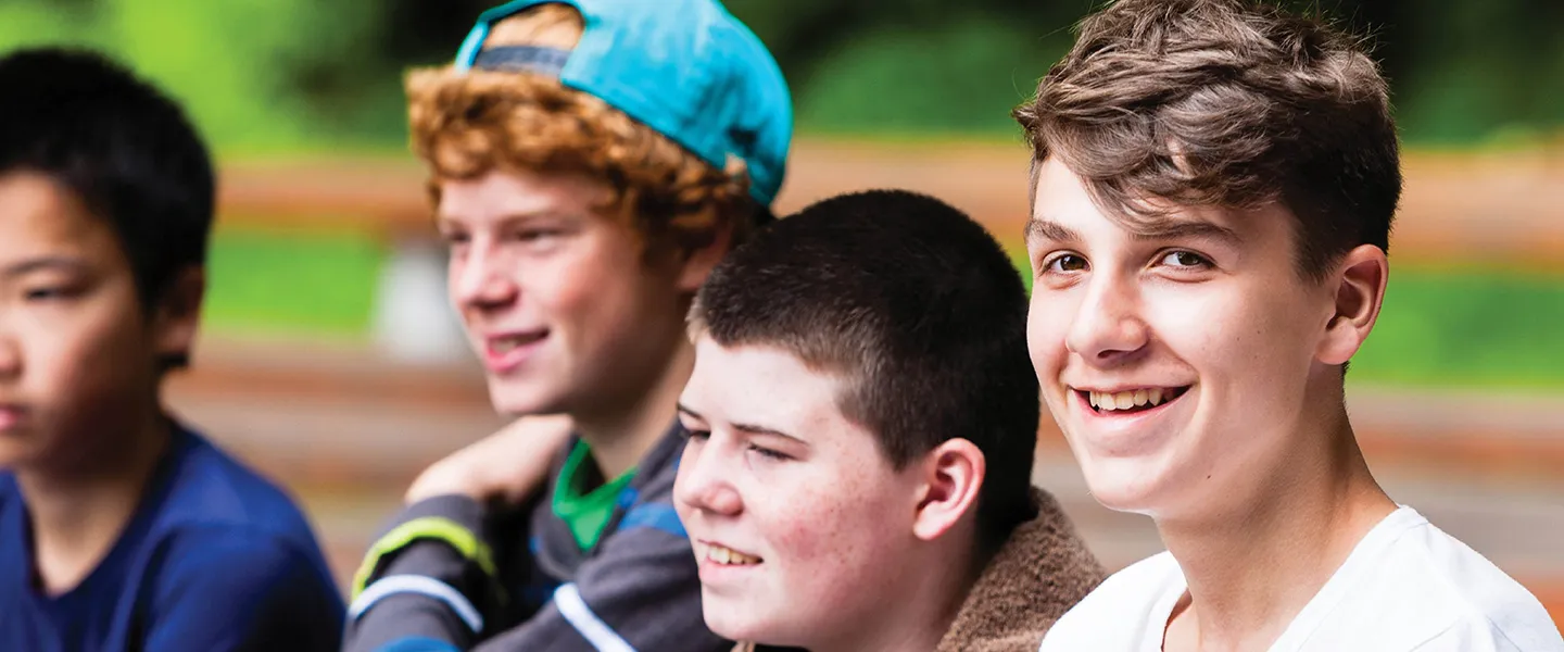 A group of teenage boys sit together in an outdoor setting.