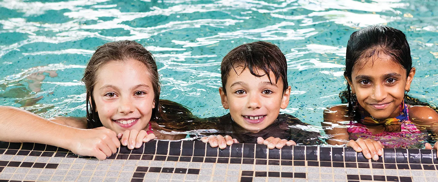 Three children at the edge of a swimming pool.