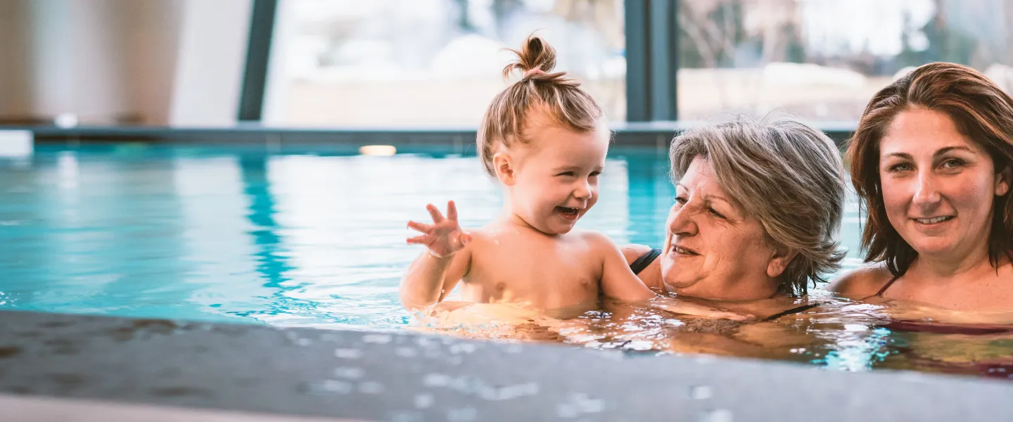 Three generations of family members play together in an indoor swimming pool