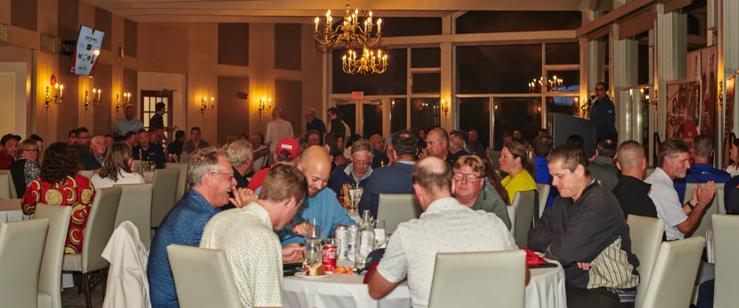 A reception hall full of people at several tables with white tablecloths.
