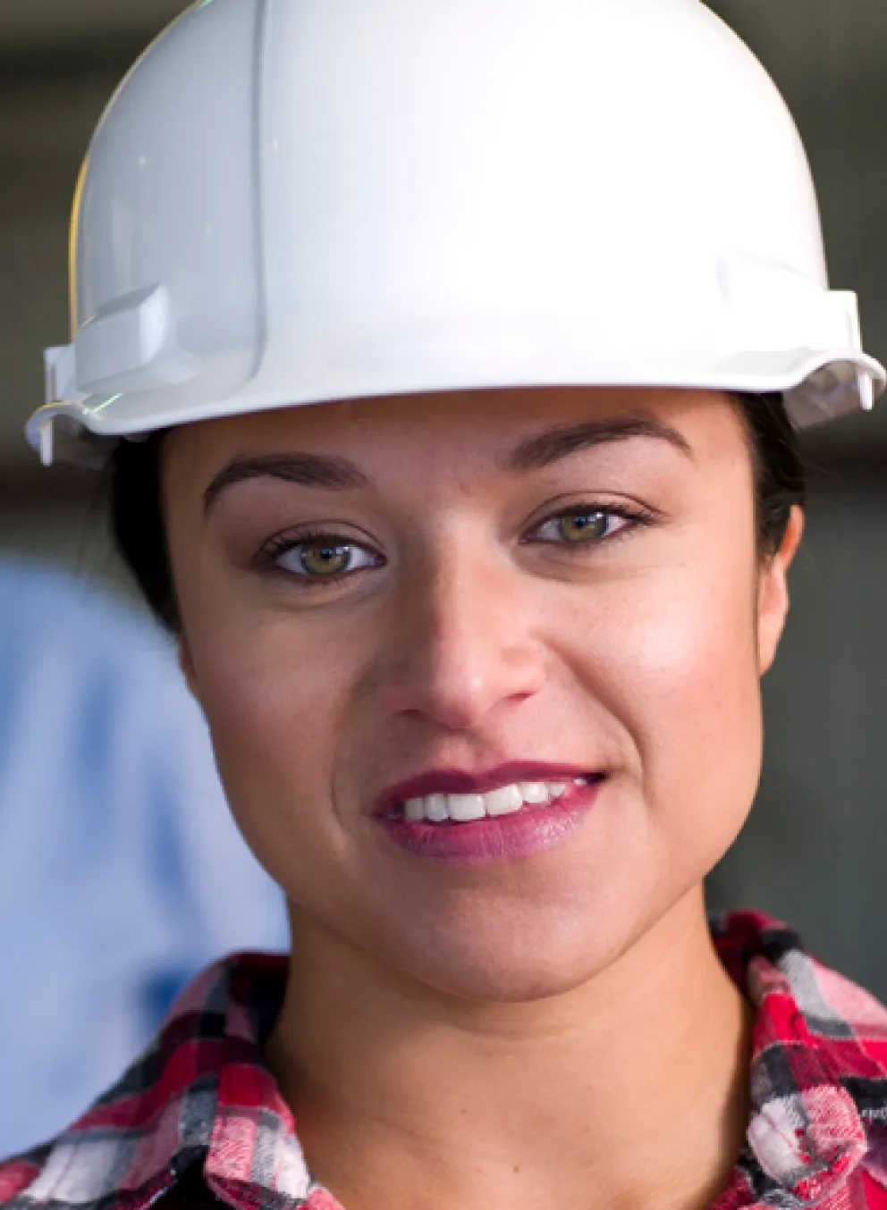 A woman wearing a white hard hat looks into the camera.