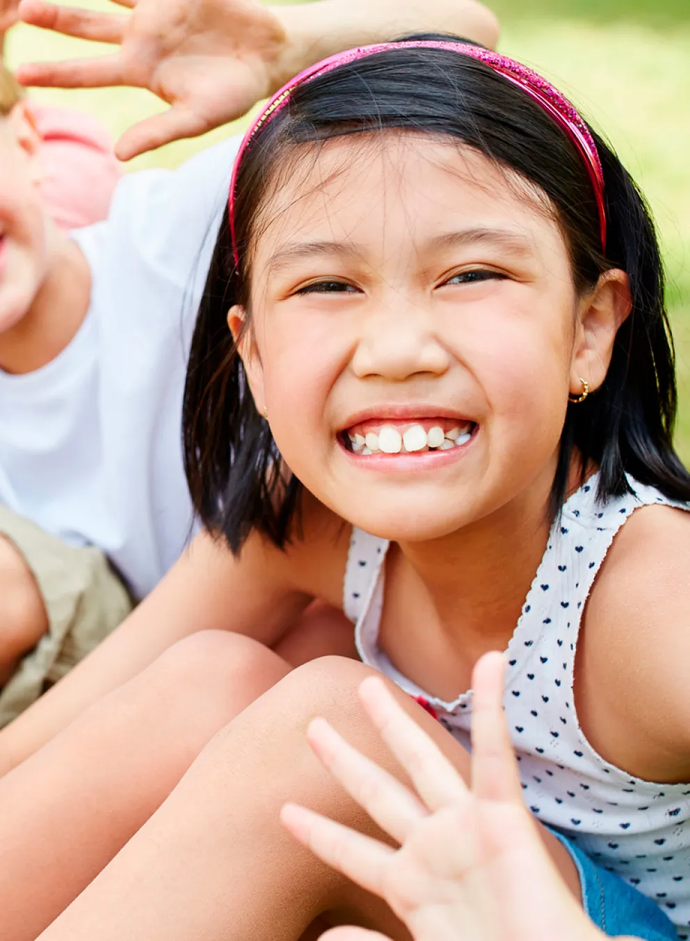 A group of children sit in a row smiling and waving.