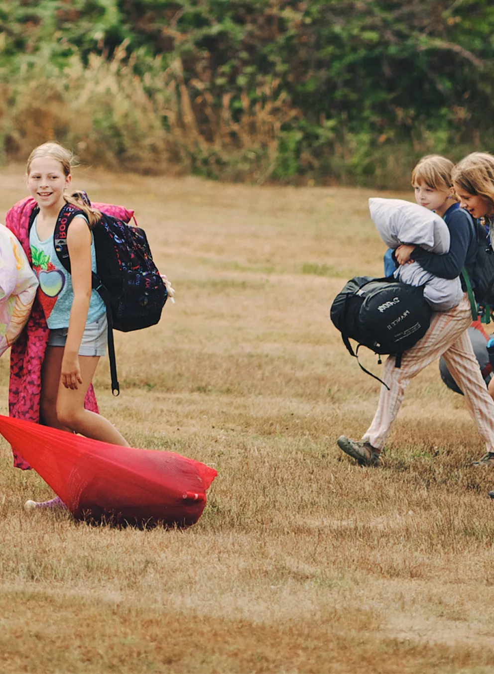 A group of campers carry pillows and sleeping bags.