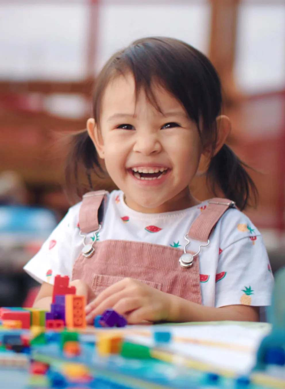 A smiling toddler sits at a table playing with toys.