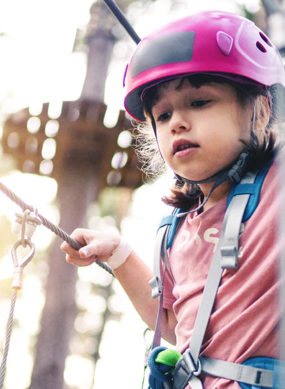 A girl wearing a helmet and safety harness navigates a high ropes course.