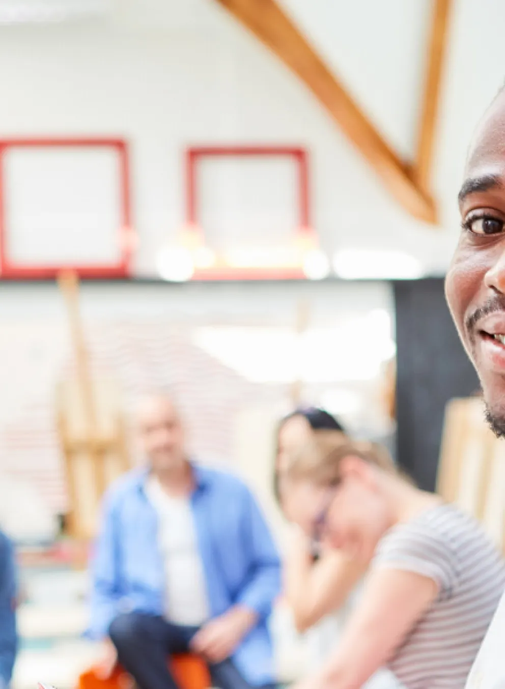 Man sits in room with other people, smiling.