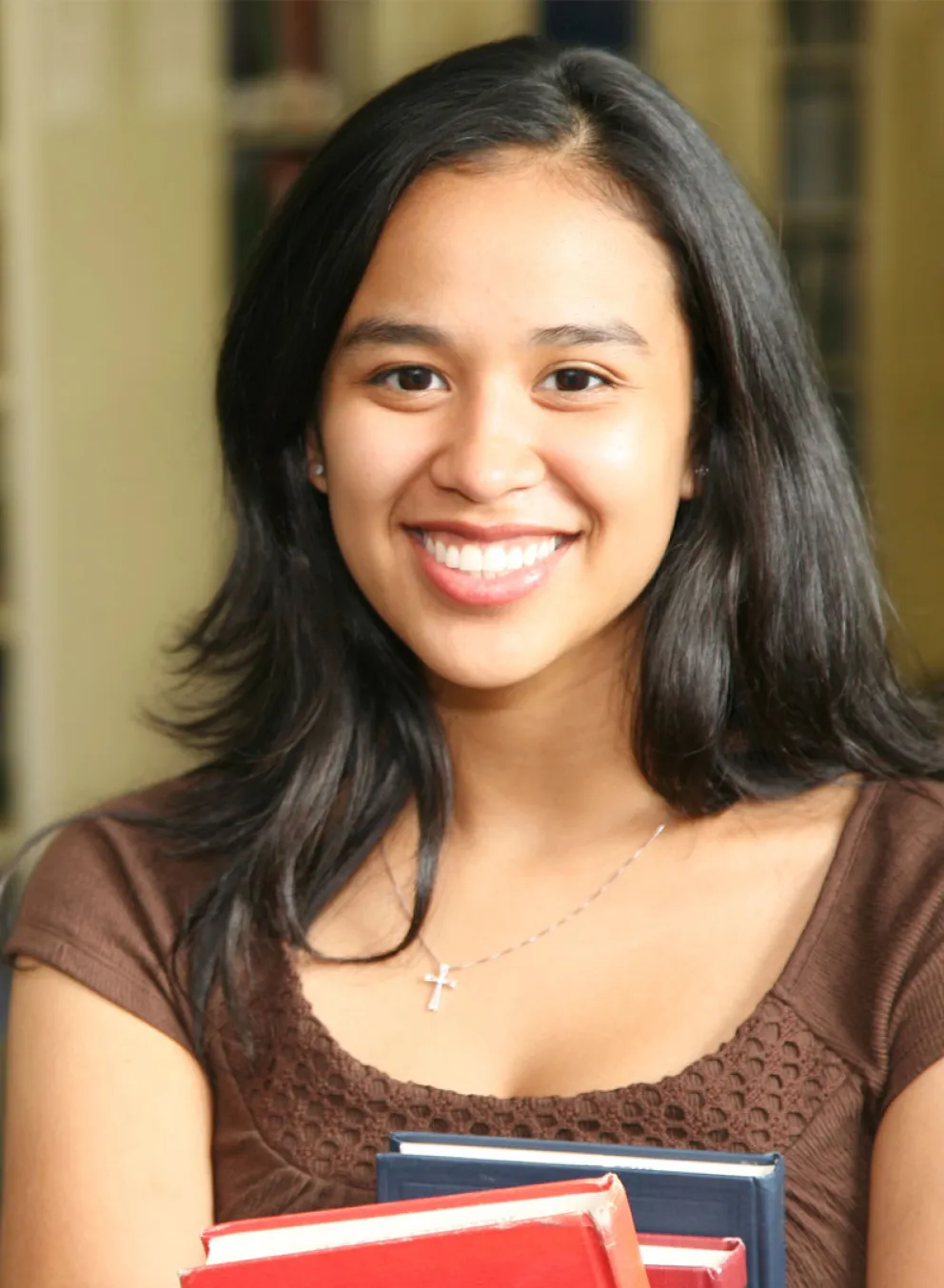 A young woman holding books in a library setting.