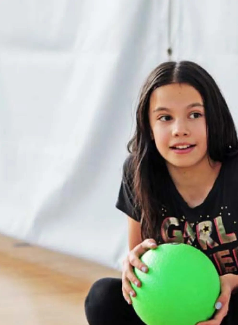 Two young girls sit in a gymnasium with a  ball.