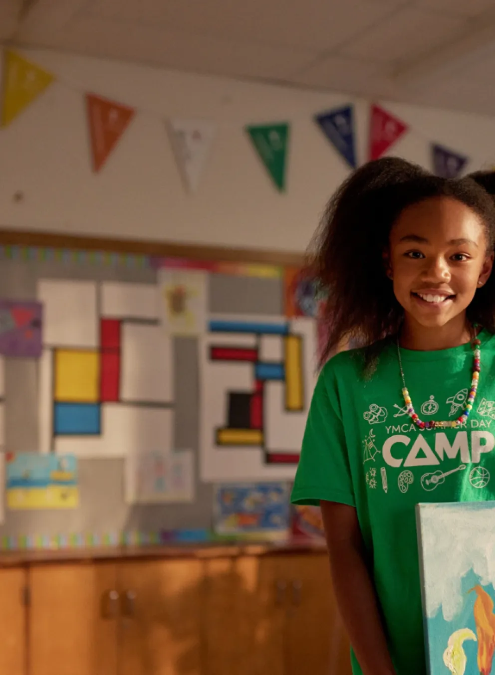 A girl in a green Camp t-shirt holding a painting