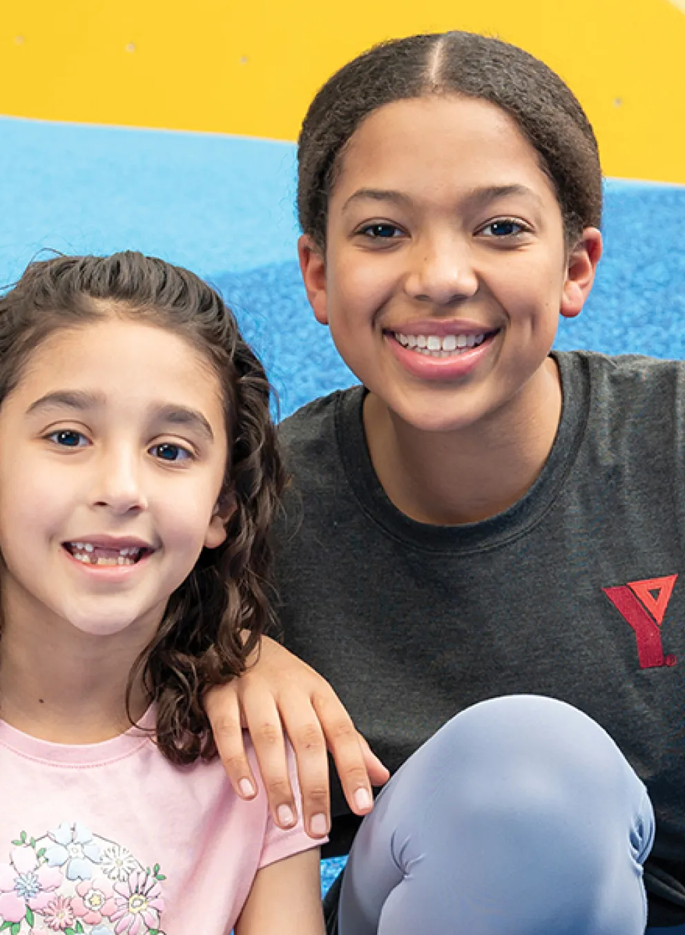 Two young girls sitting on a slide in a gym, smiling and enjoying their playtime together.