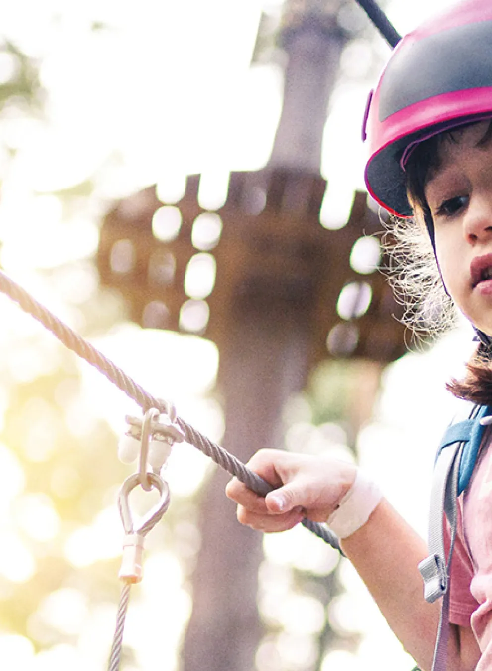 A young girl navigates a rope course among the trees in a wooded area, showcasing her adventurous spirit.