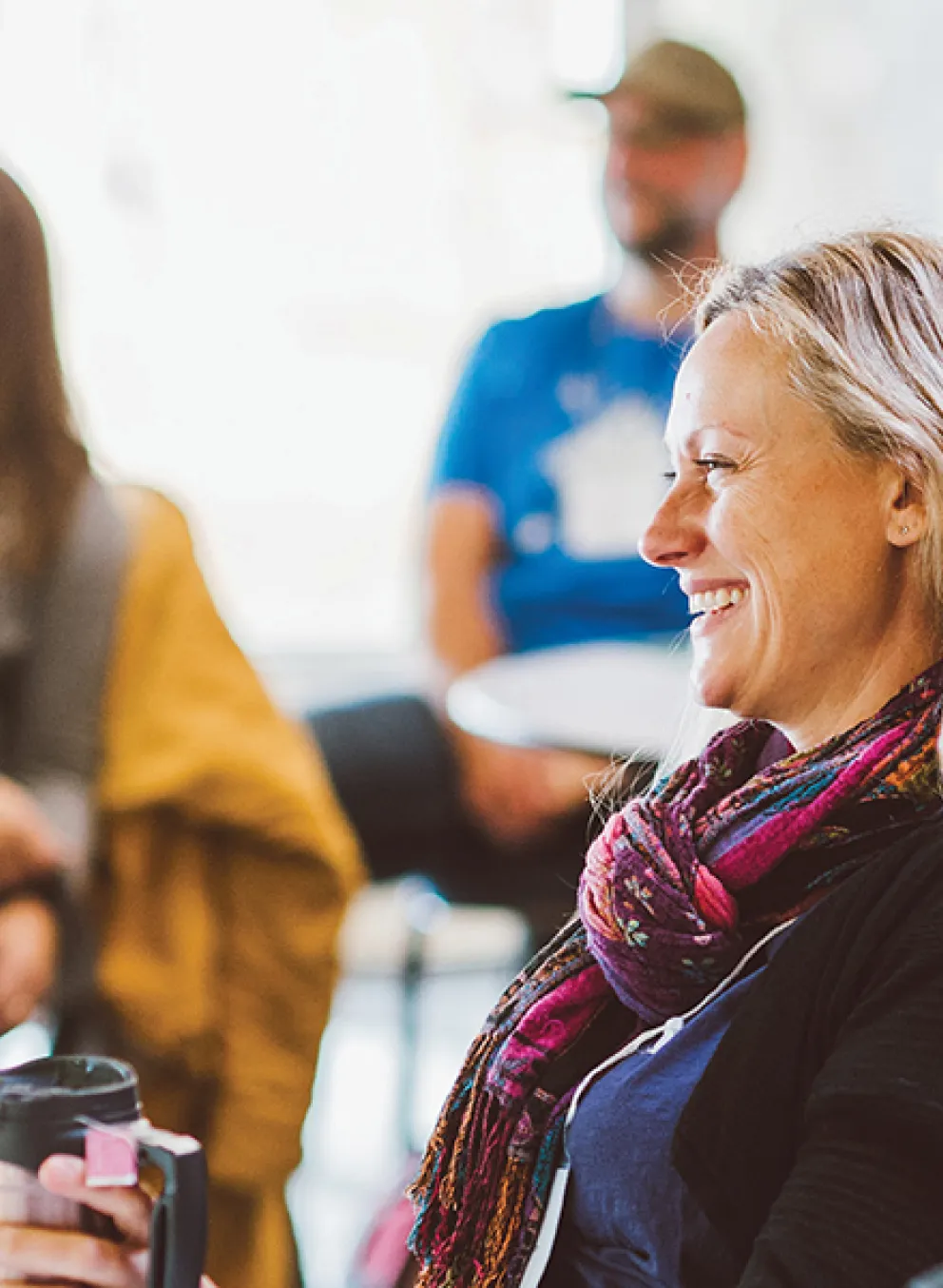 A diverse group of people sitting at tables in a bright room, smiling and engaged