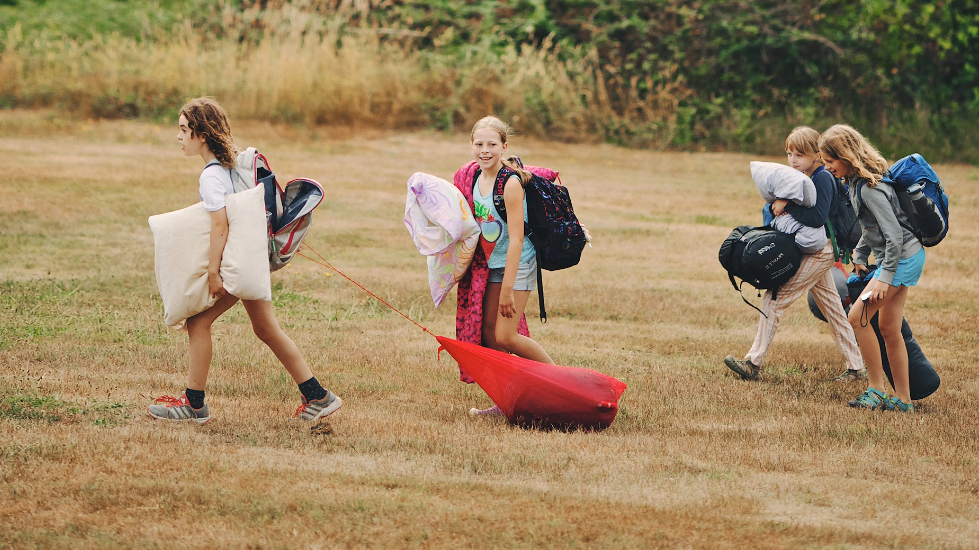 A group of campers carry pillows and sleeping bags.