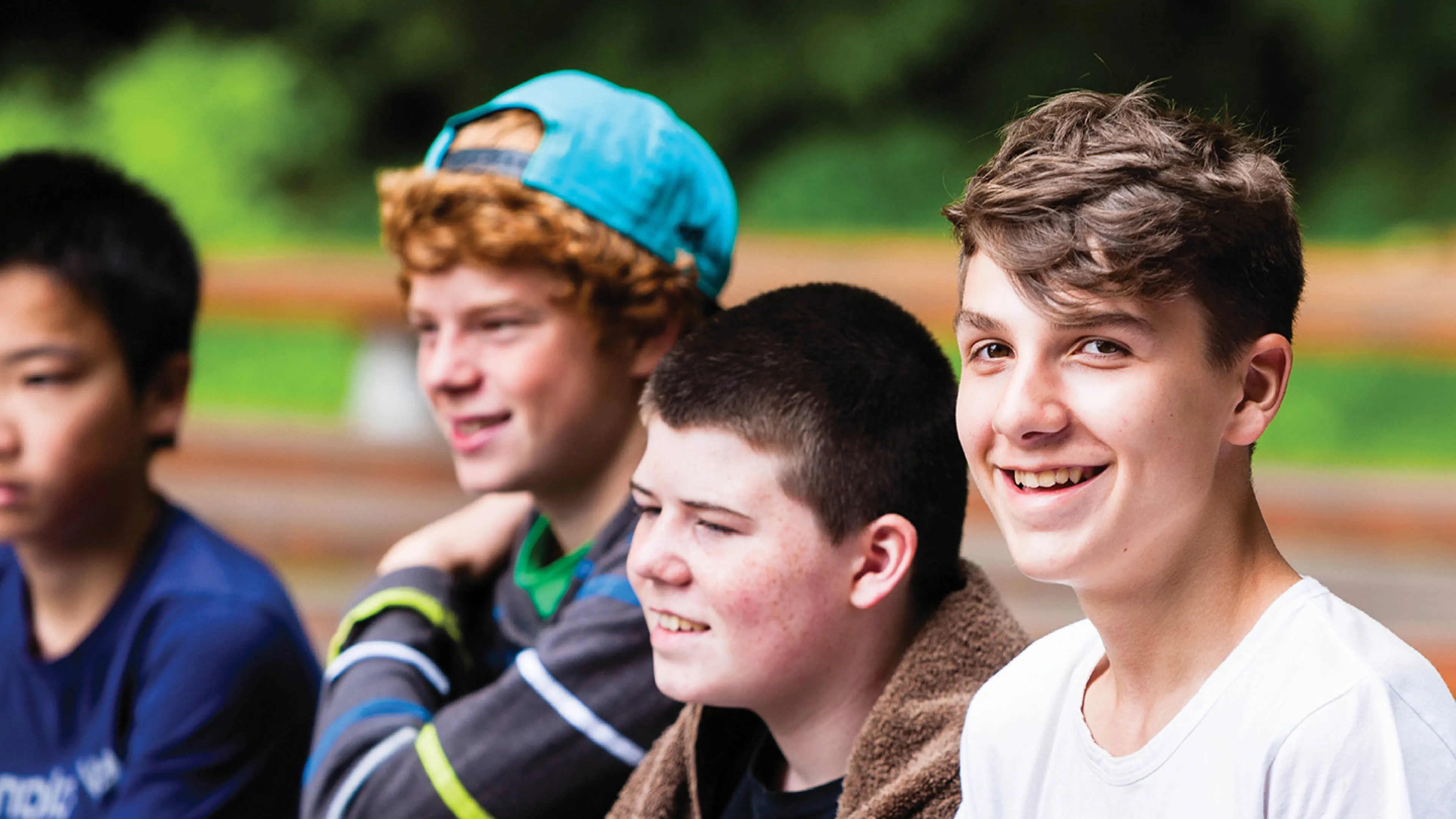 A group of teenage boys sit together in an outdoor setting.