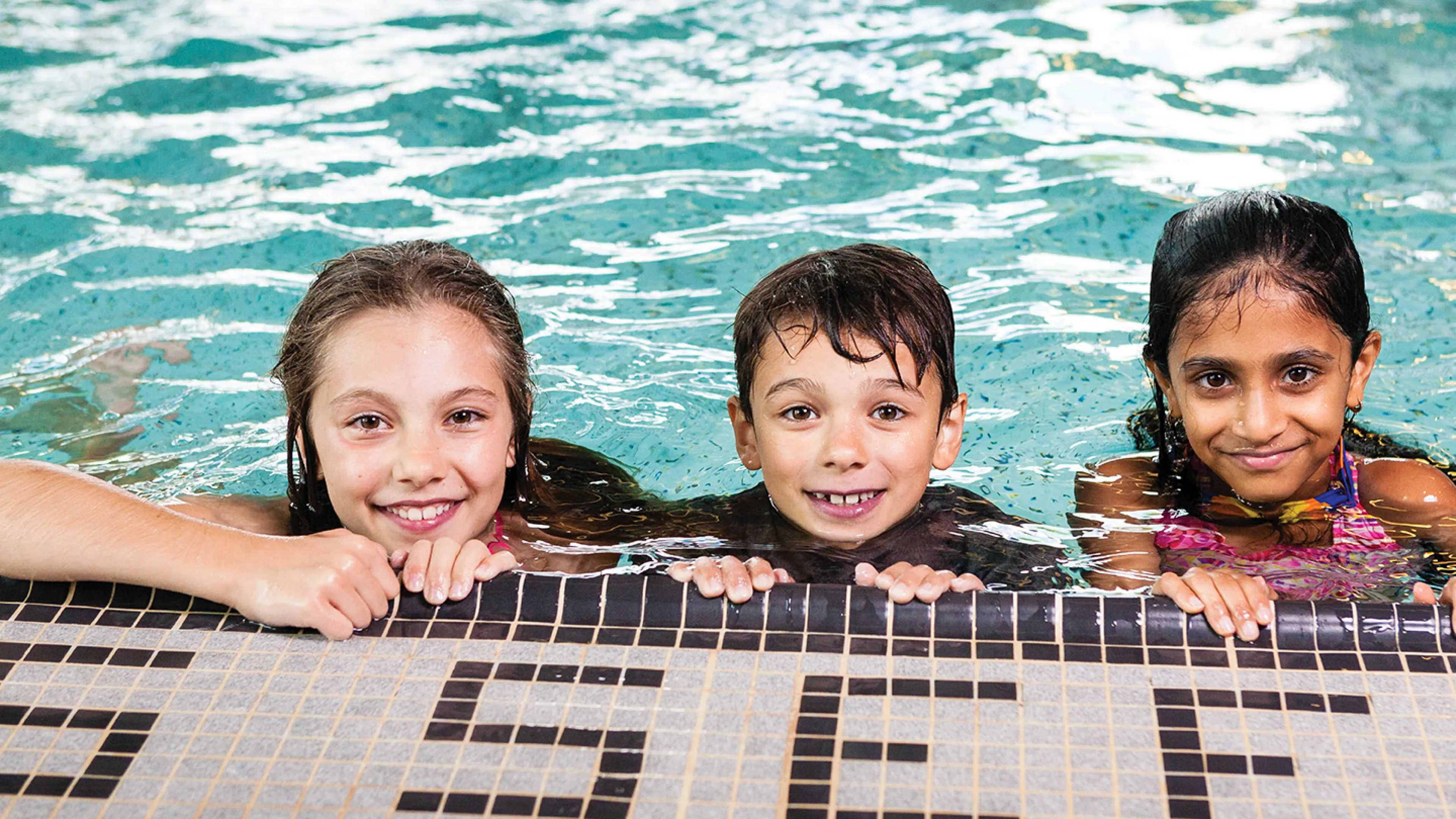 Three children at the edge of a swimming pool.