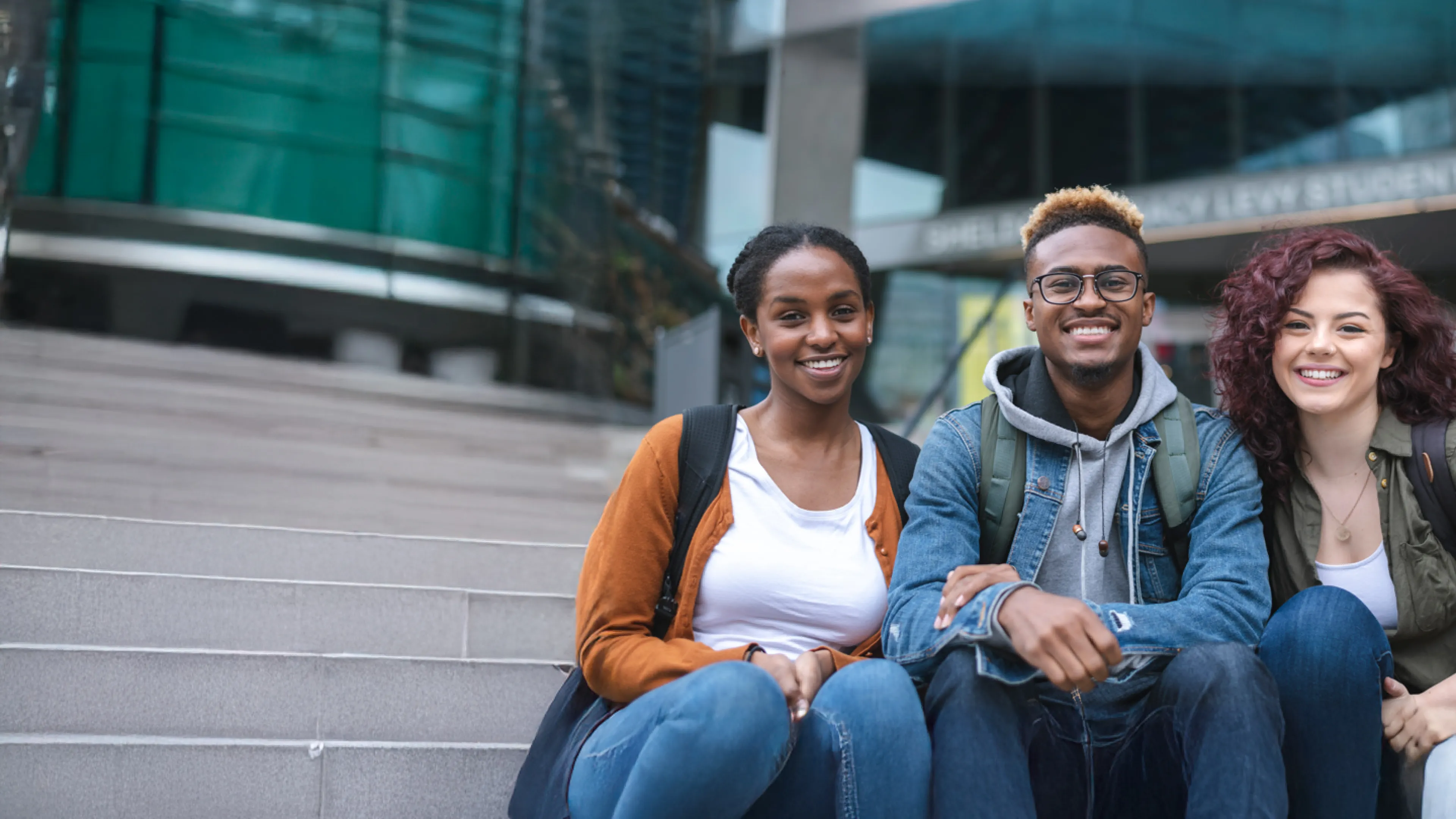 Three diverse youth sit on steps.
