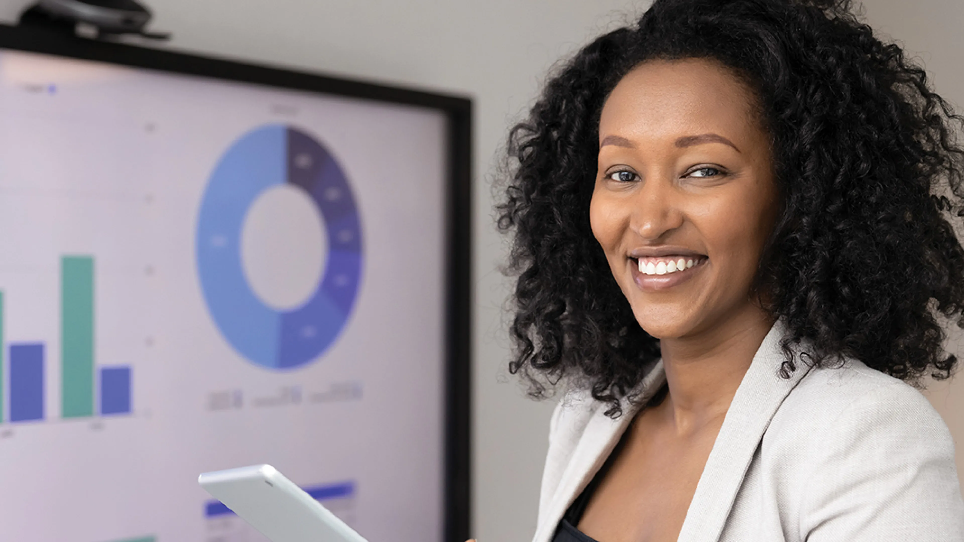 A woman stands holding a tablet in front of a whiteboard, engaged in a presentation or discussion.