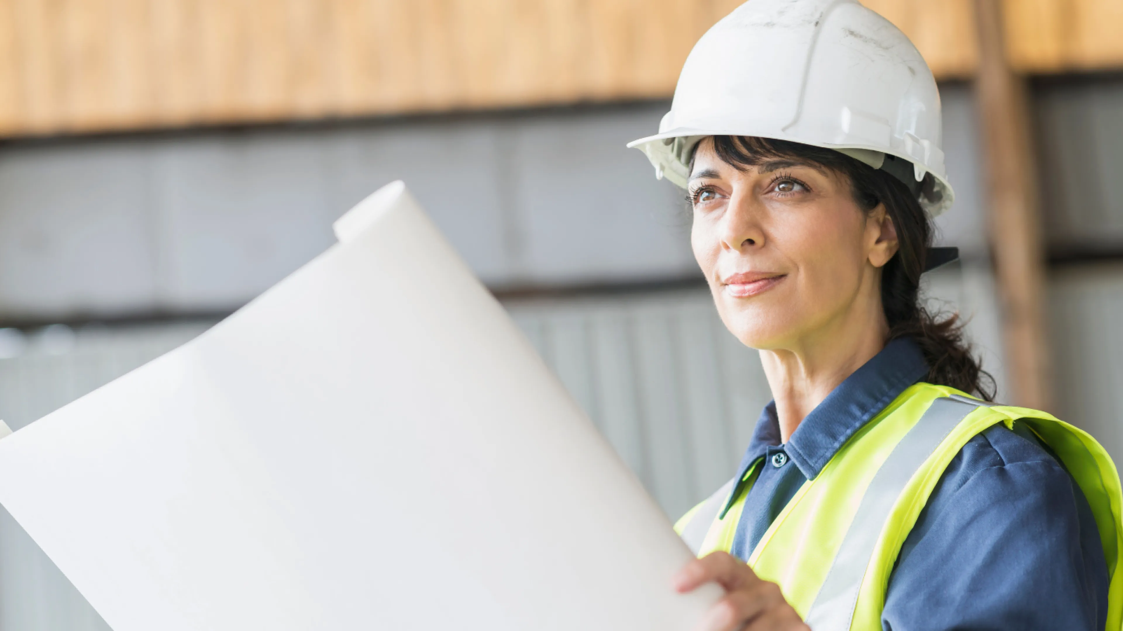 A woman in construction gear, holding a large blueprint