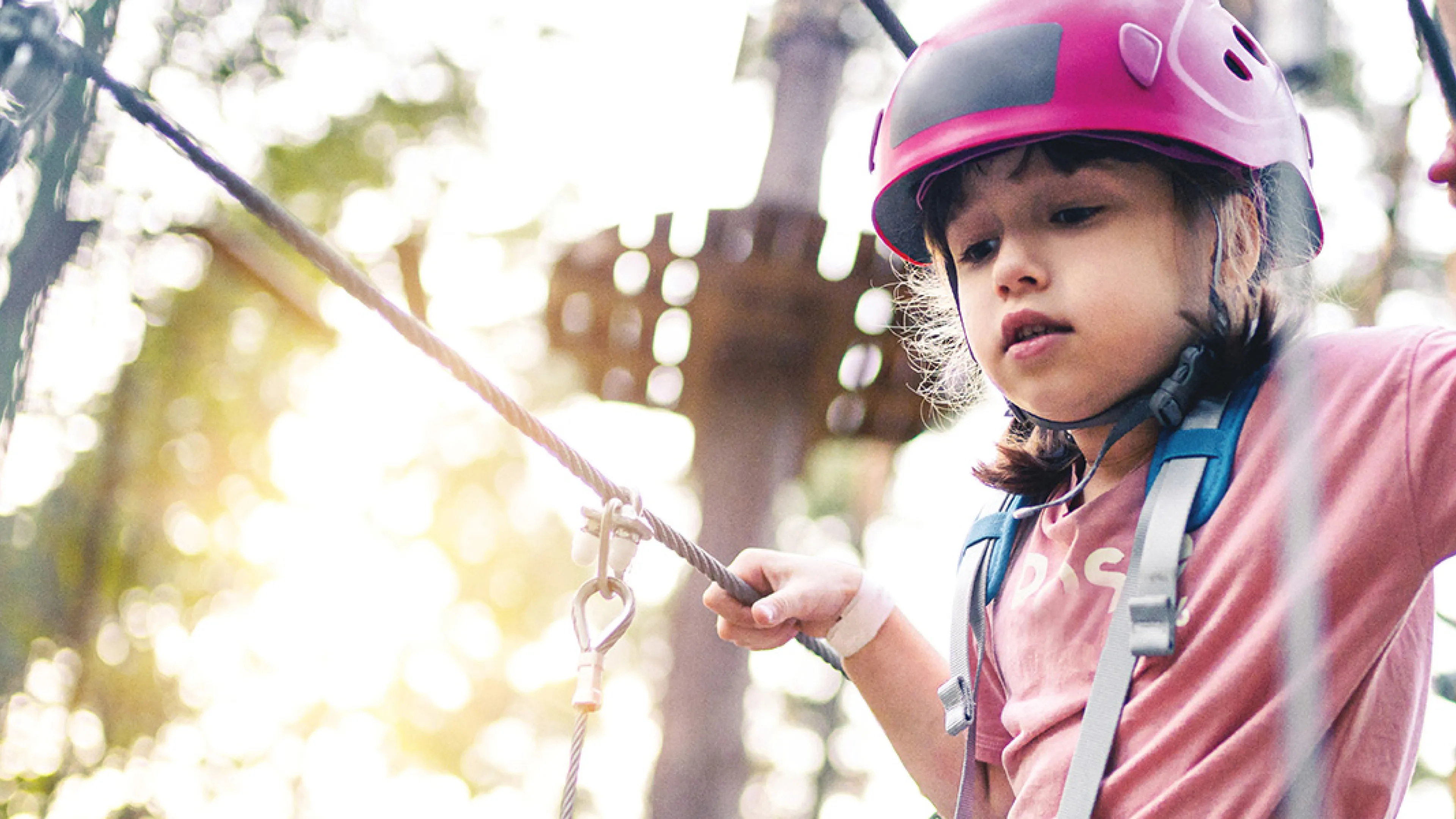 A young girl navigates a rope course among the trees in a wooded area, showcasing her adventurous spirit.