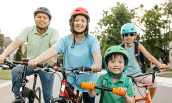 A happy family of four wearing helmets are biking outdoors.