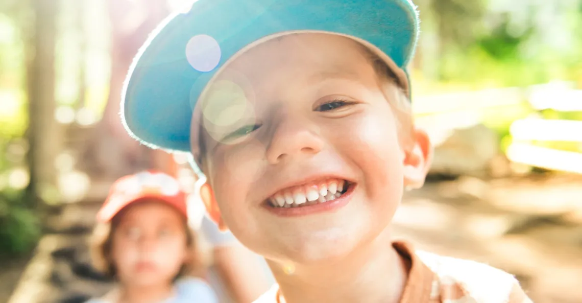 A young boy wearing a baseball cap smiles into the camera.