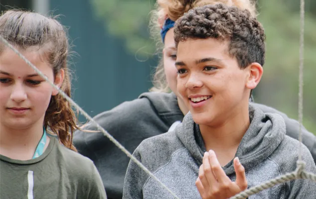 A group of teens work together to solve a team challenge involving ropes.