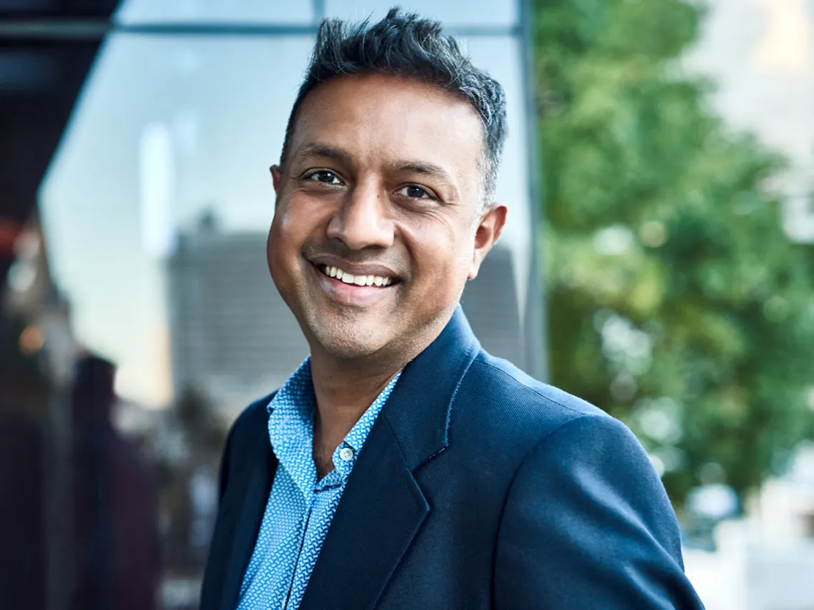 A smiling man stands outside the entrance to an office building.