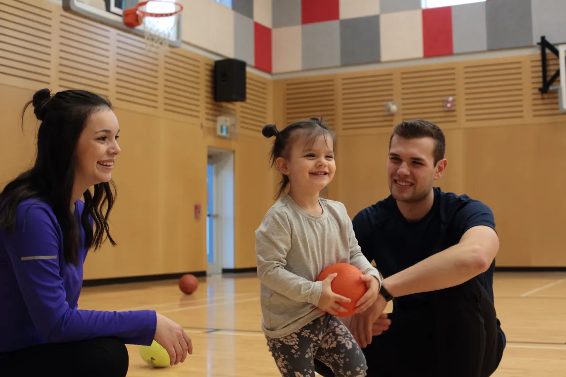 Two adults and a child holding a basketball in a gymnasium
