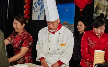 A chef and three other people preparing and serving food at the Chinese food booth.