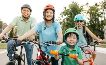 A happy family of four wearing helmets are biking outdoors.