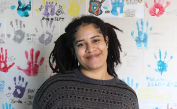 Y youth housing client Ica standing and smiling in front of a wall covered in colourful handprints