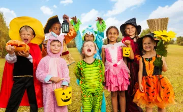 Eight children in various Halloween costumes posing in a field